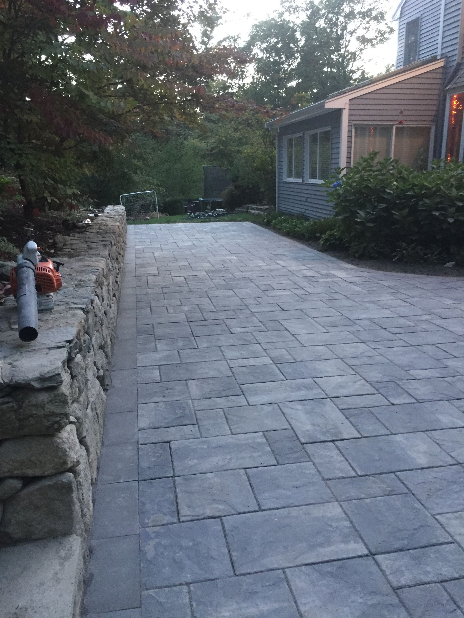 A brick driveway leading to a house with trees in the background.