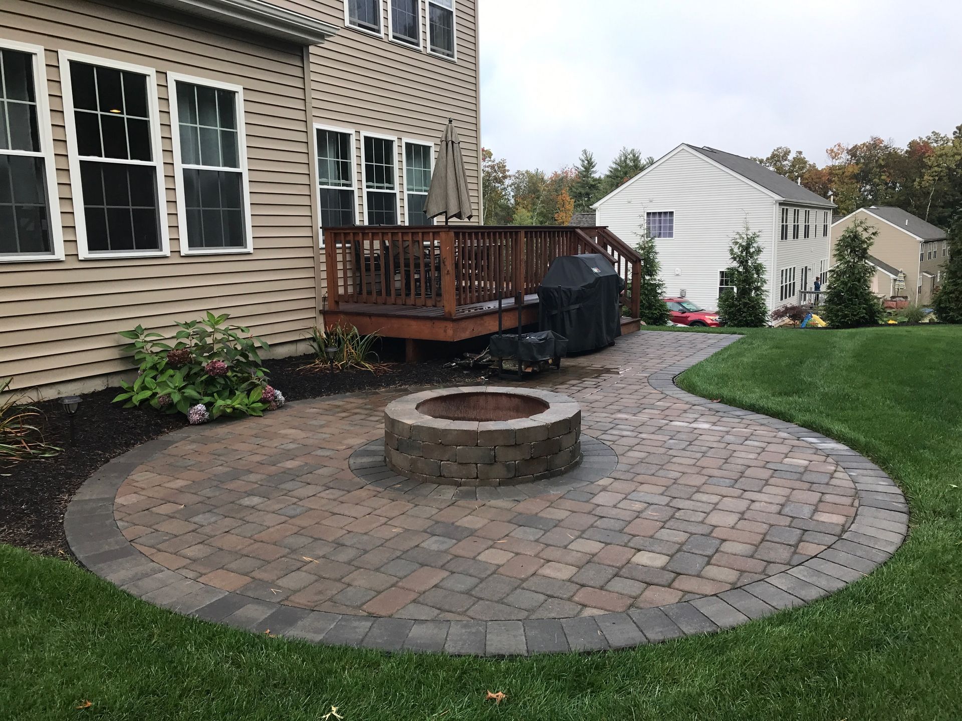 A fire pit is in the middle of a patio in front of a house.