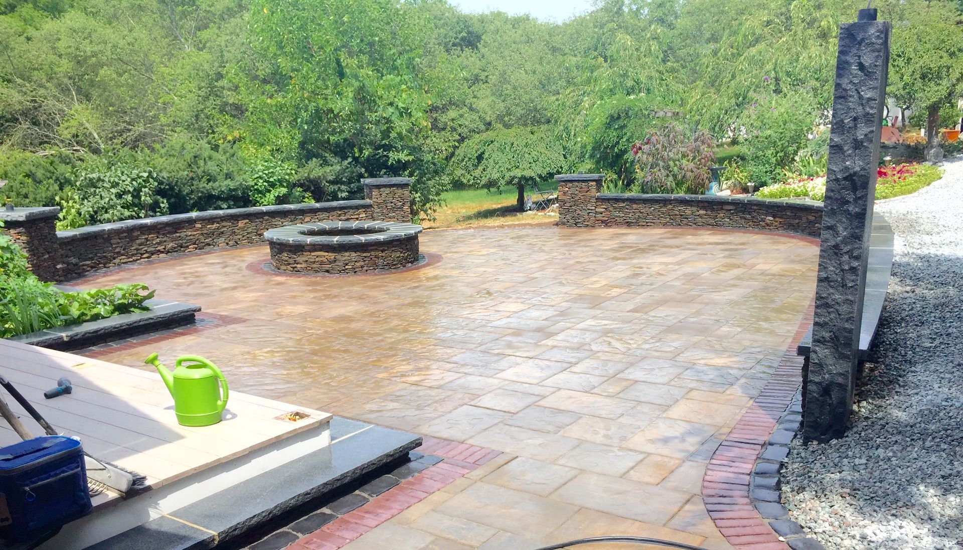 A green watering can is sitting on a patio next to a fire pit.
