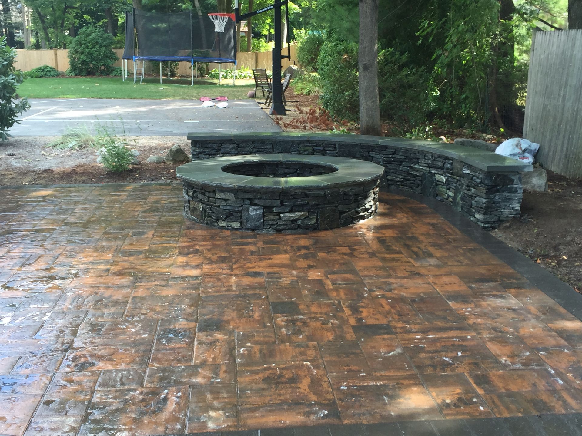 A brick patio with a fire pit and a trampoline in the background