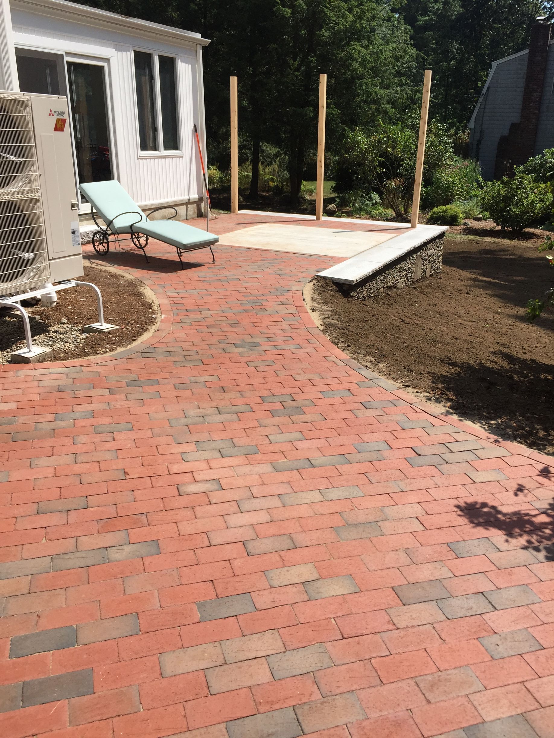 A brick patio with chairs and a bench in front of a house.