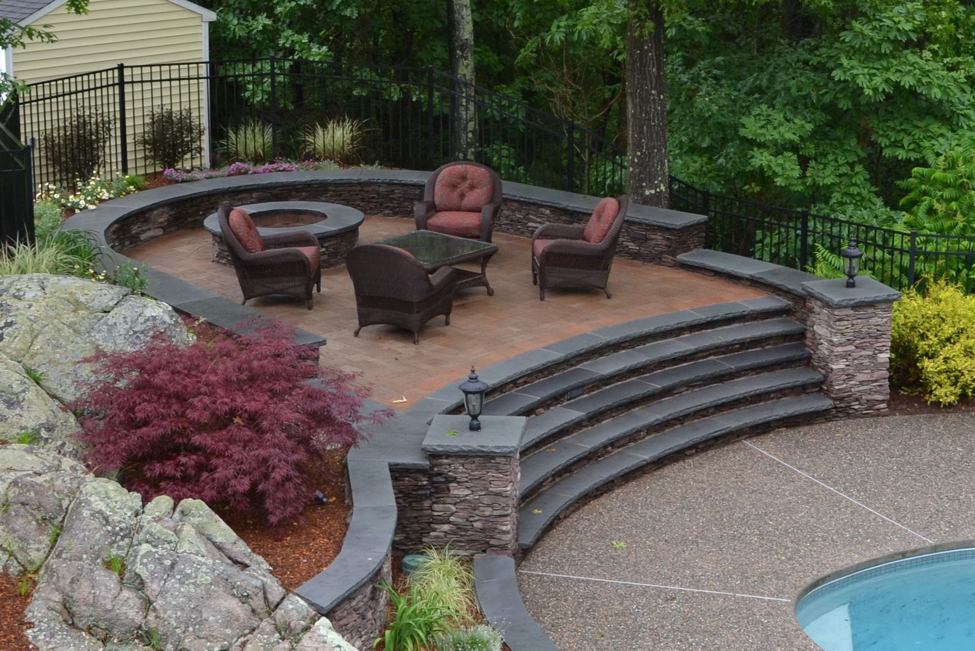 A patio with chairs and a fire pit next to a pool