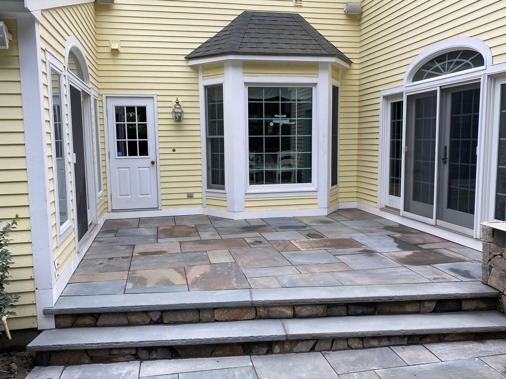 A yellow house with a stone patio in front of it.