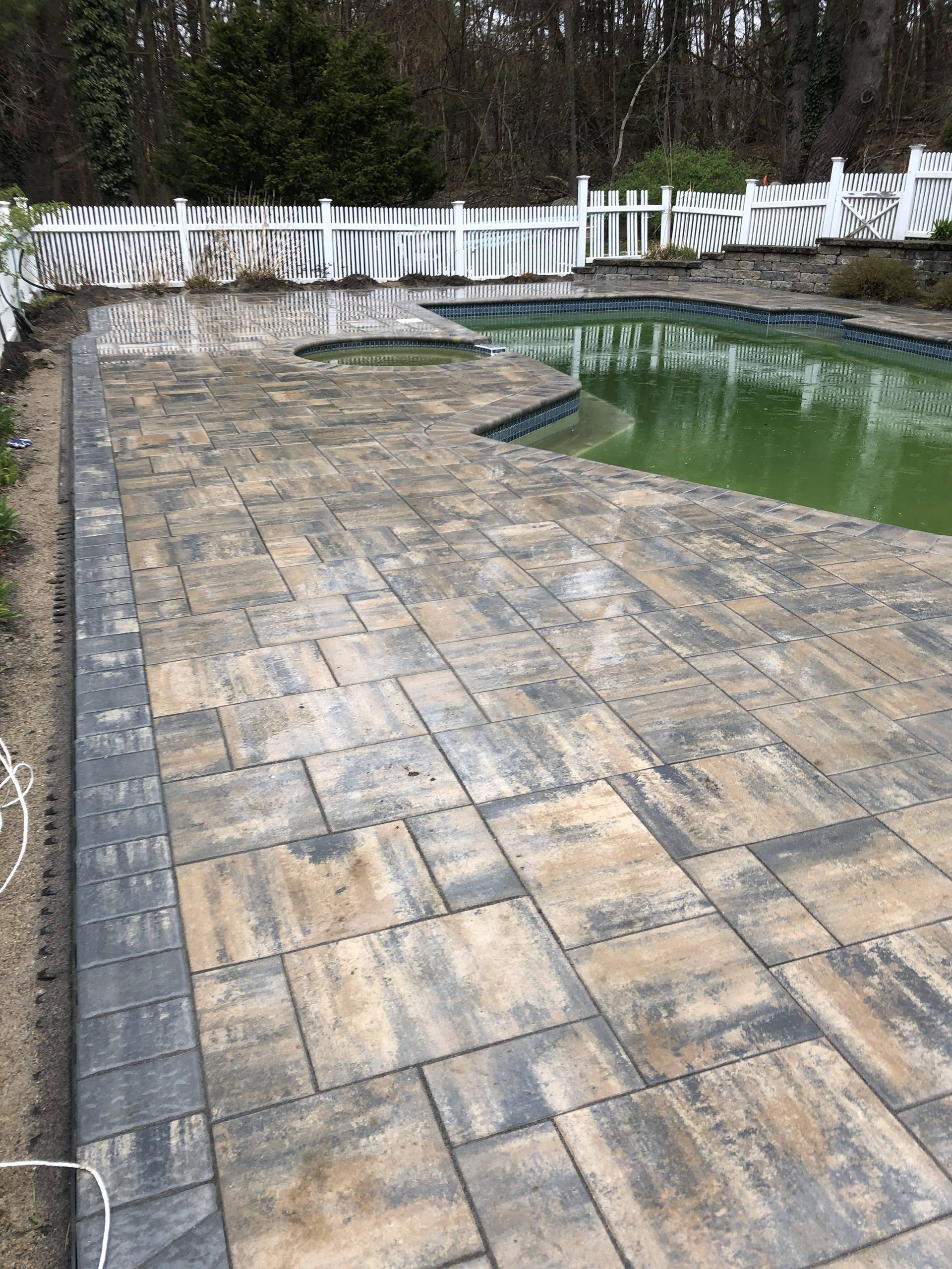 A patio with a pool in the background and a white fence.