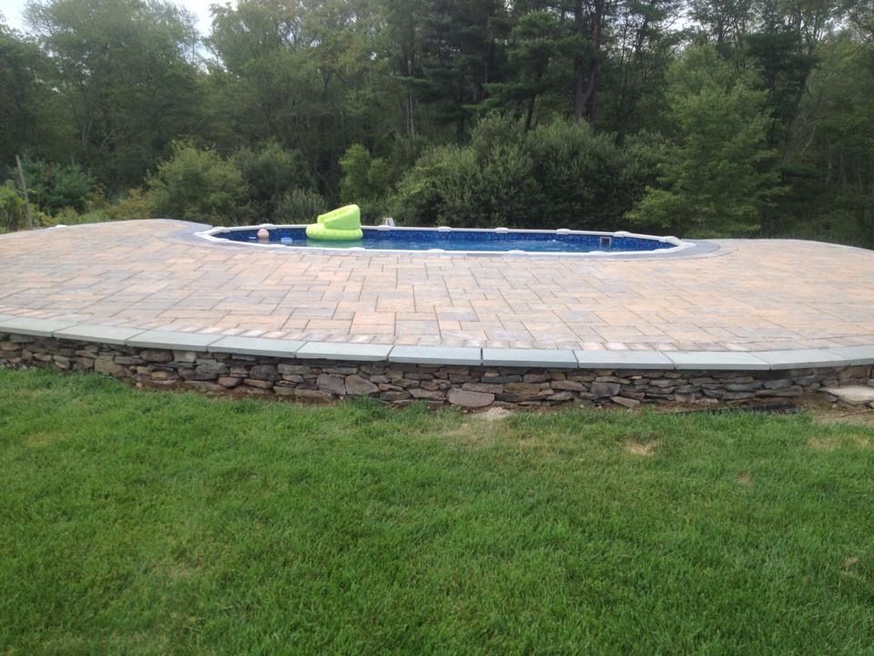 A swimming pool is surrounded by a stone wall and a brick patio.