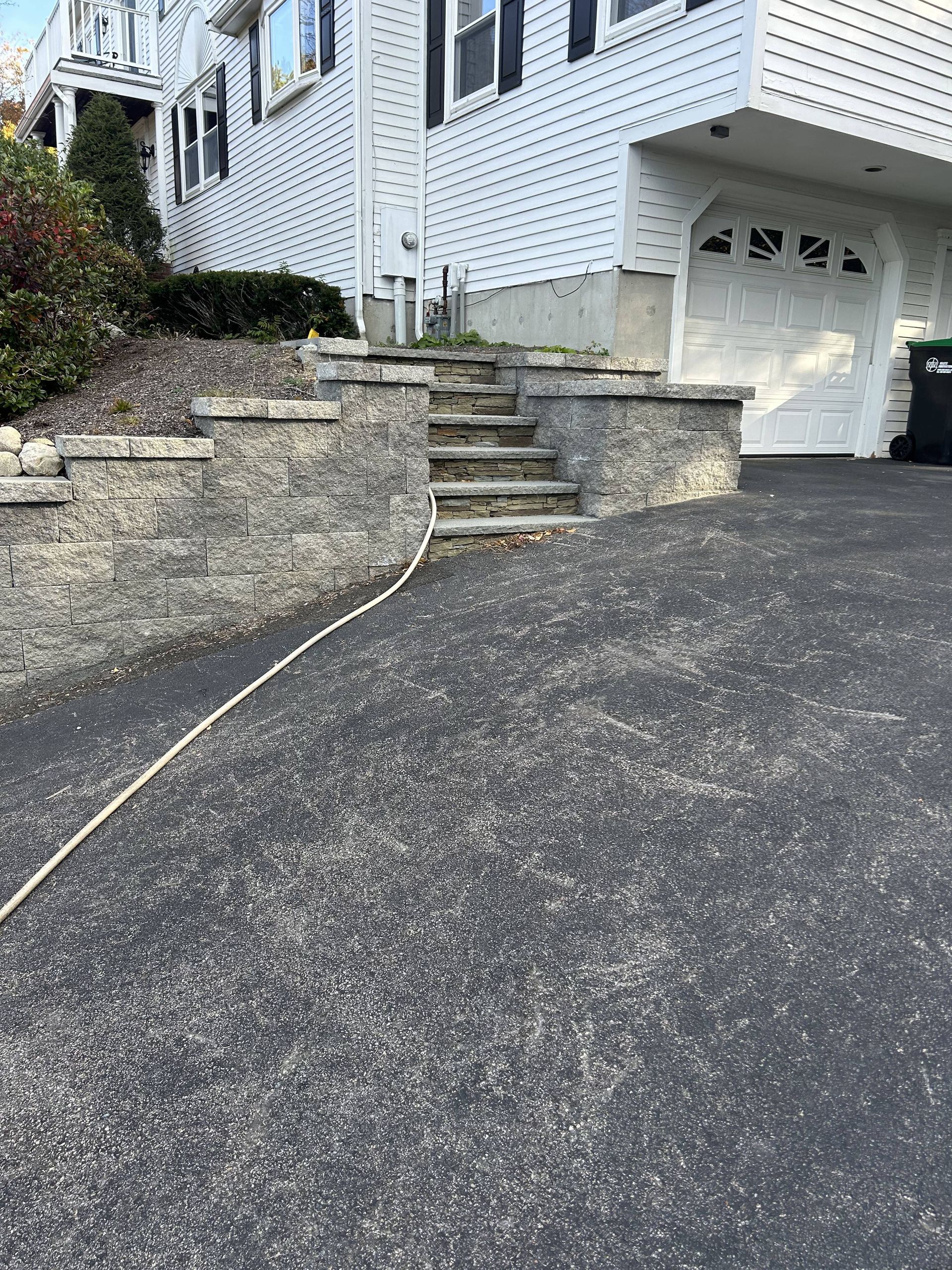 A driveway leading up to a house with stairs and a trash can.