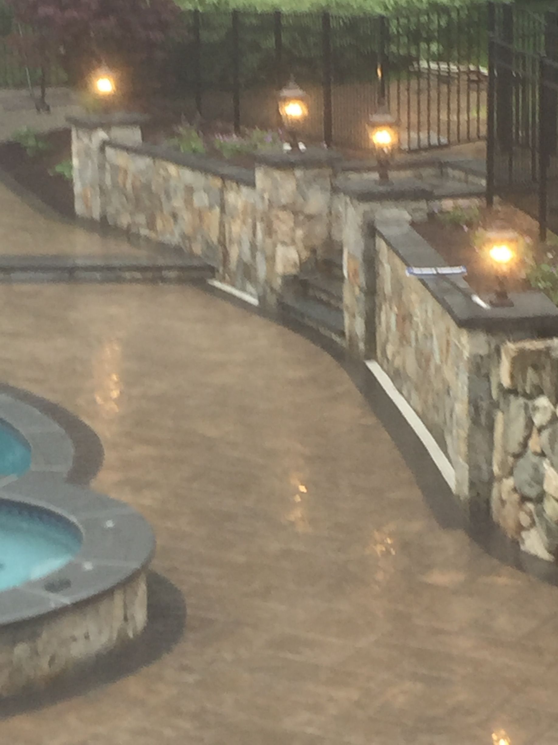 A swimming pool is surrounded by a stone wall and a fence.
