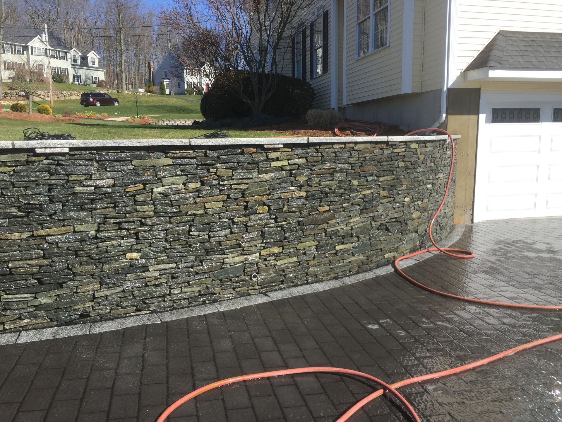 A stone wall is being cleaned with a hose in front of a house.
