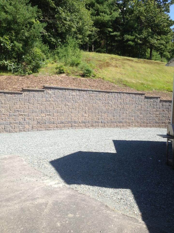 A brick wall surrounds a gravel driveway with trees in the background