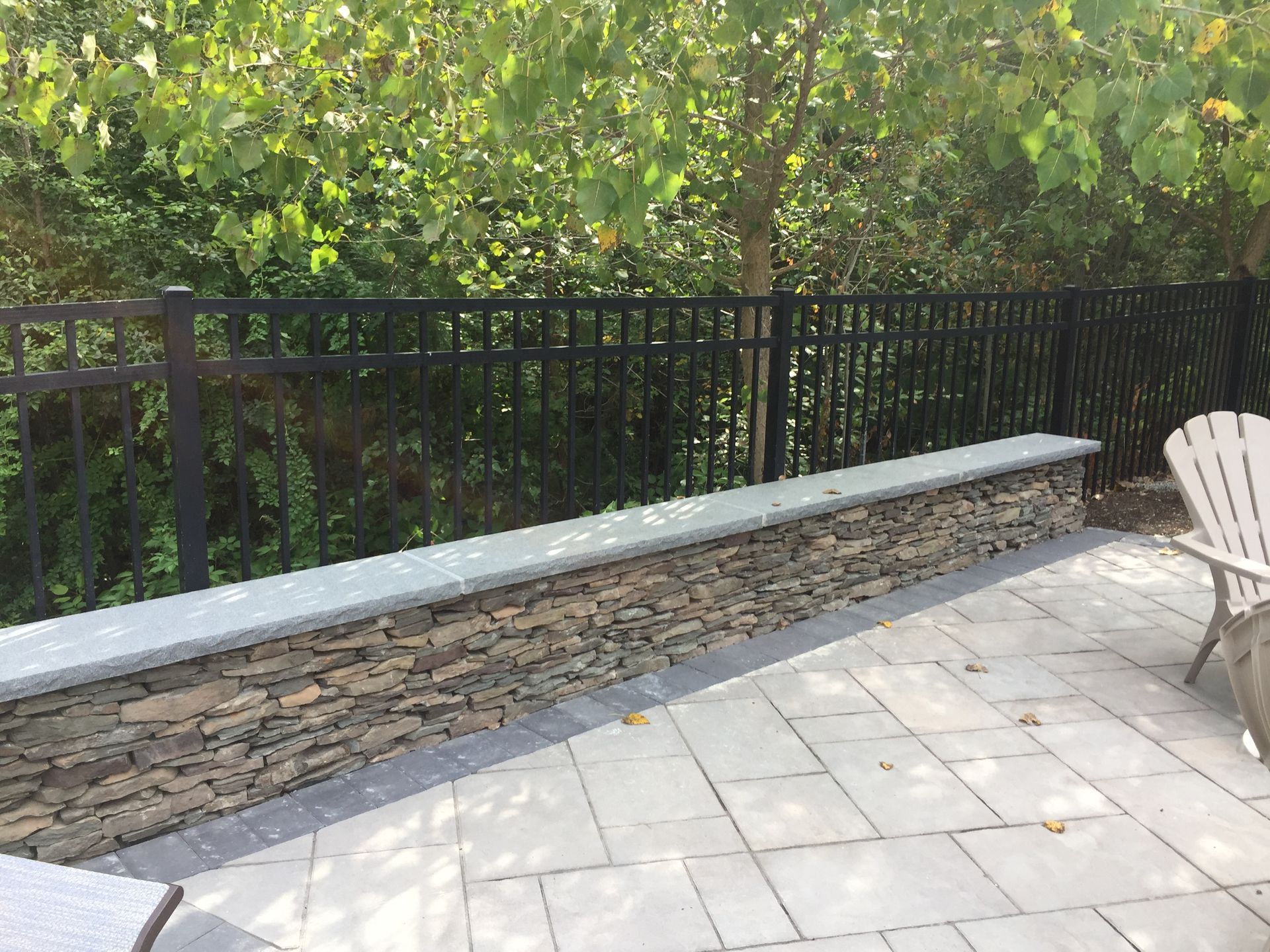 A patio with a stone wall , chairs and a fence.