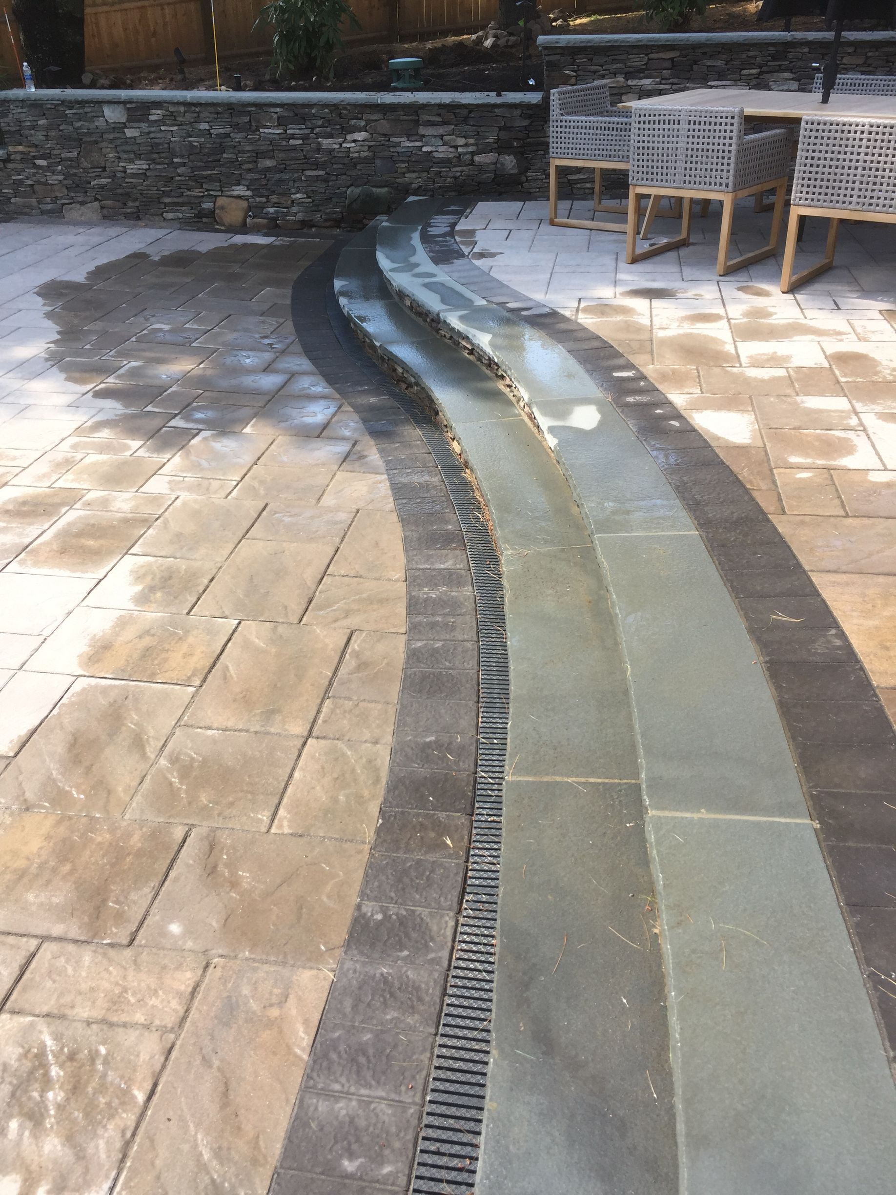 A drain on the side of a patio next to a table and chairs.