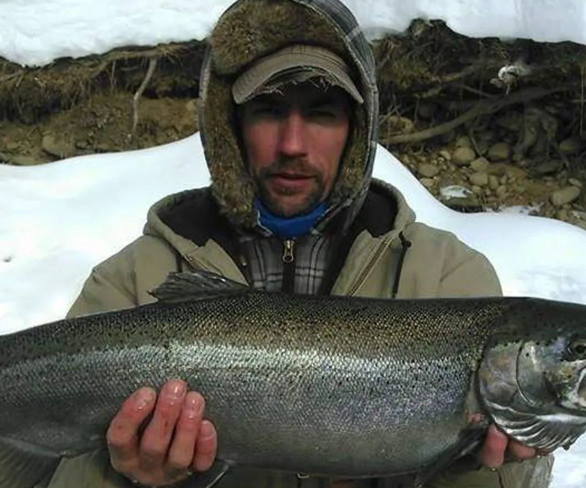 A man in a fur hat is holding a large fish