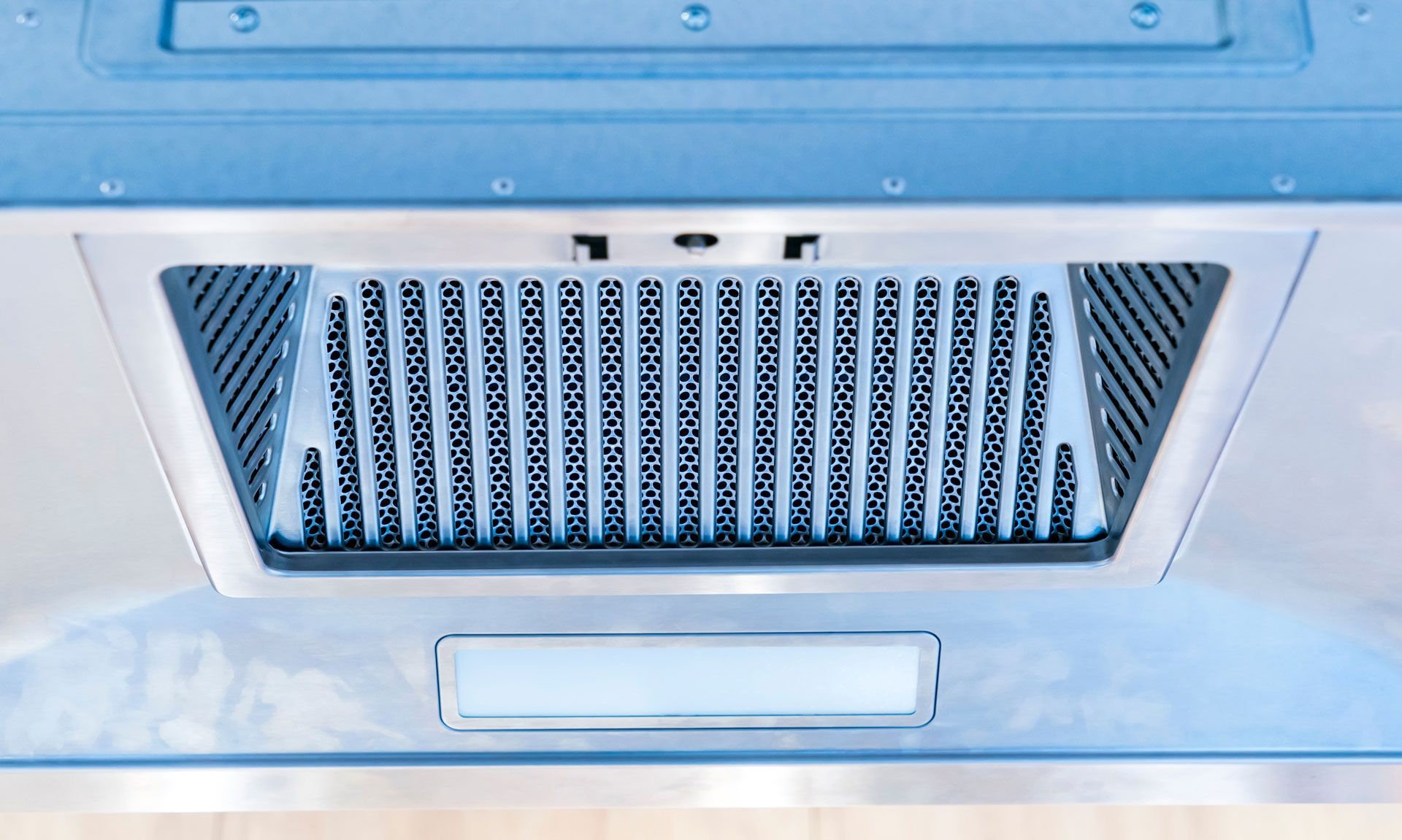 A close-up view of the underside of a stainless steel range hood, showing a vertical baffle filter and light panel.