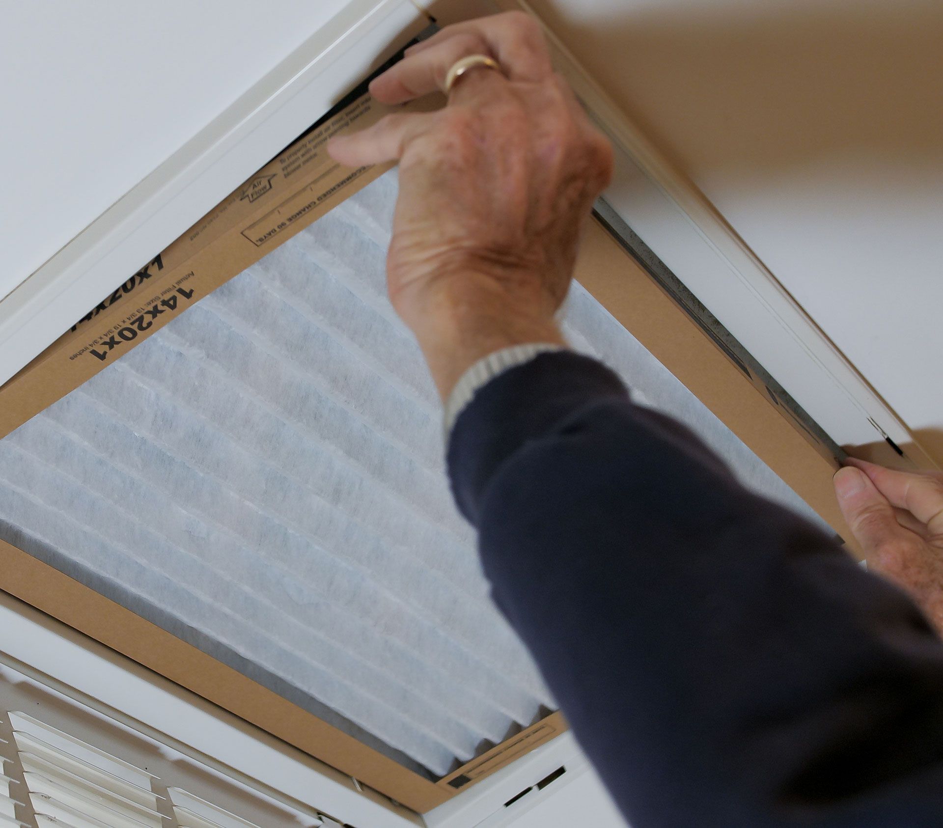 A person installing a new rectangular air filter into a ceiling-mounted HVAC vent.