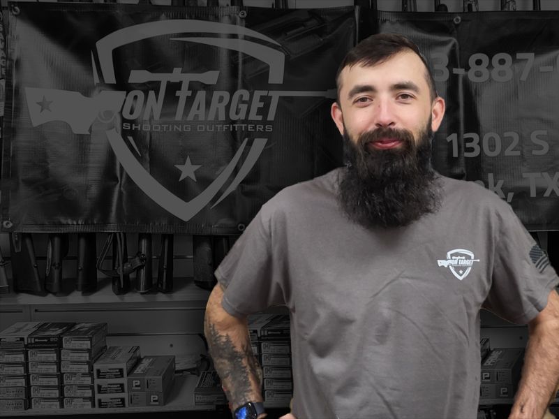 A man with a beard is standing in front of a sign that says iron target