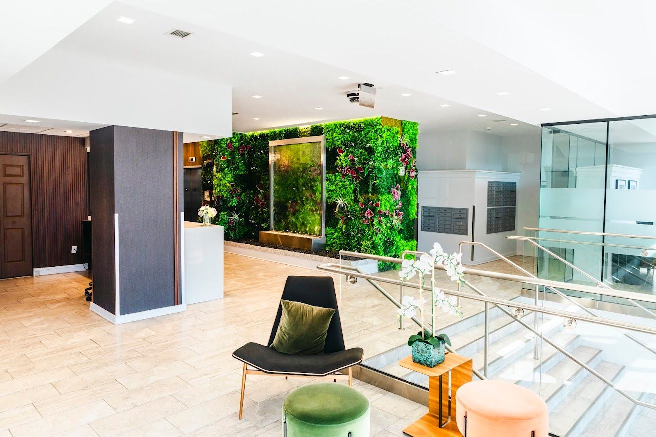 A lobby with a chair and ottomans in front of a green wall.