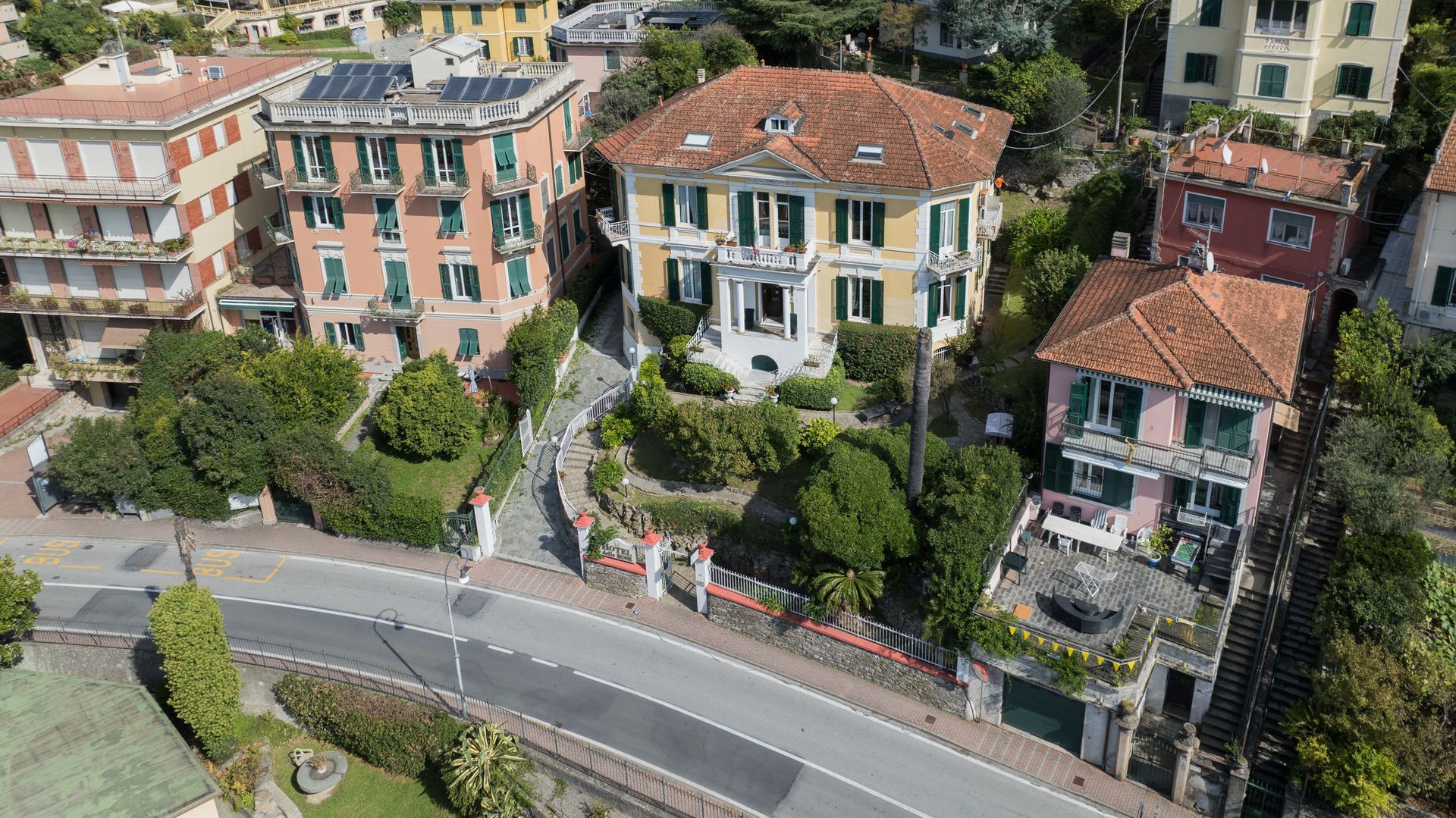 Case e strada in una soleggiata cittadina costiera con tetti arancioni, gialli e rossi.