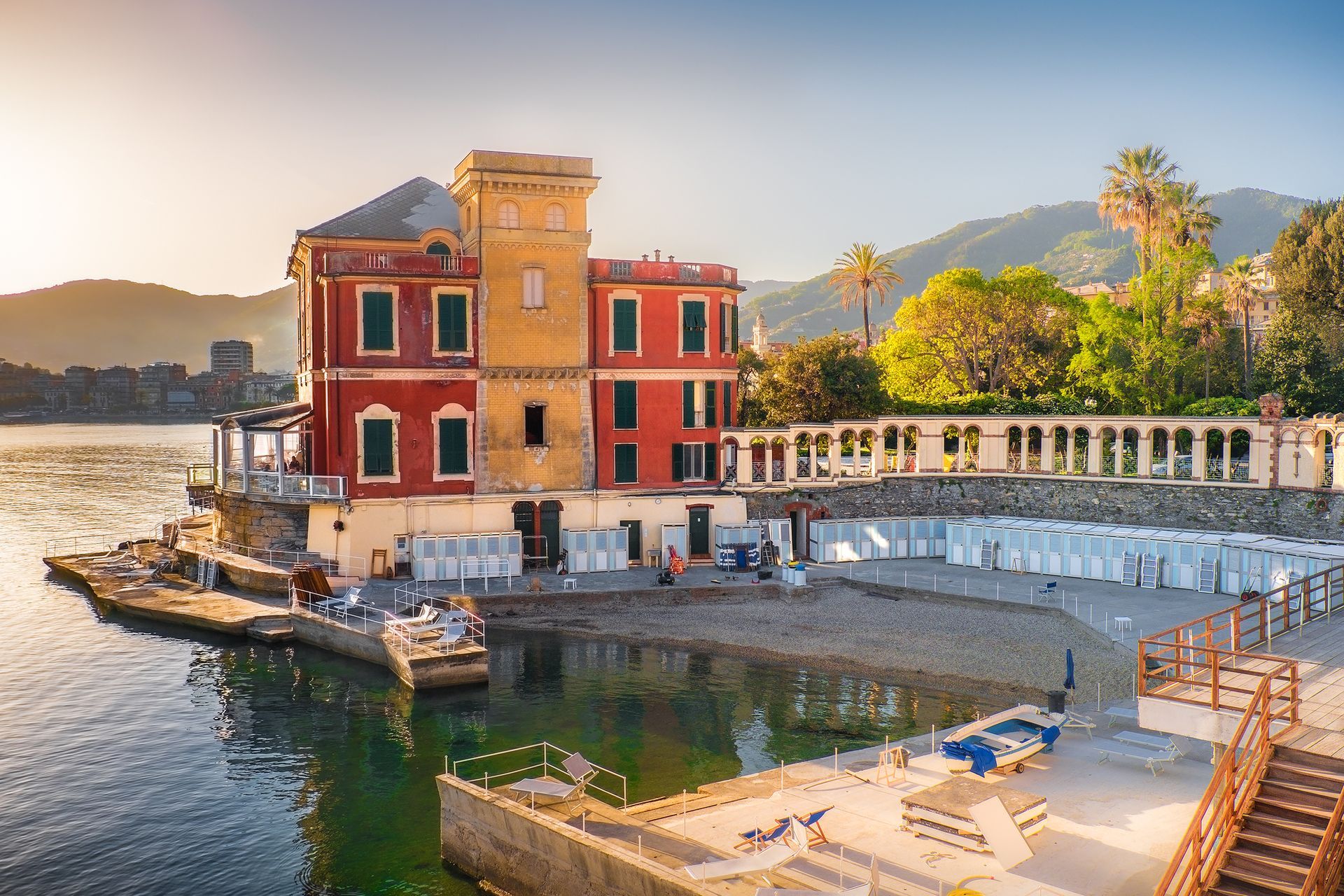 Vista da un balcone con pilastri bianchi che si affaccia su un paesaggio verde, edifici e un cielo azzurro nuvoloso.