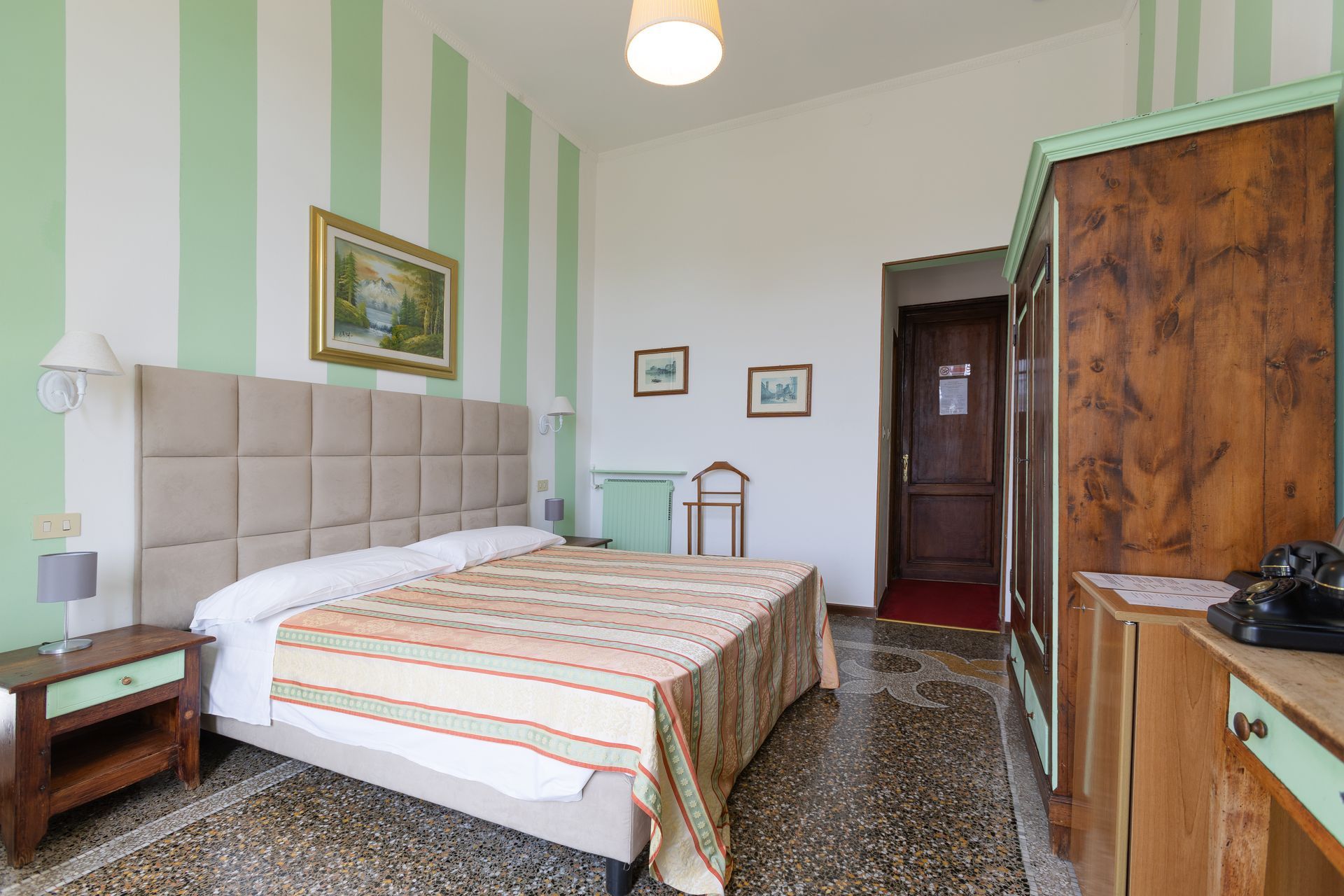 Camera d'albergo con pareti verdi a strisce, letto, mobili in legno e copriletto a fantasia.