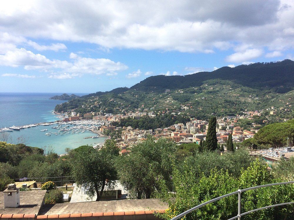 Città costiera incastonata tra montagne e mare. Porto pieno di barche sotto un cielo azzurro.