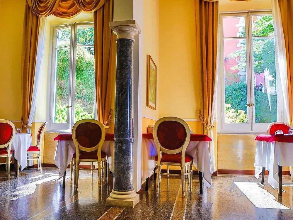 Elegante sala da pranzo con tavoli disposti vicino a grandi finestre, pavimento in marmo e colonna.