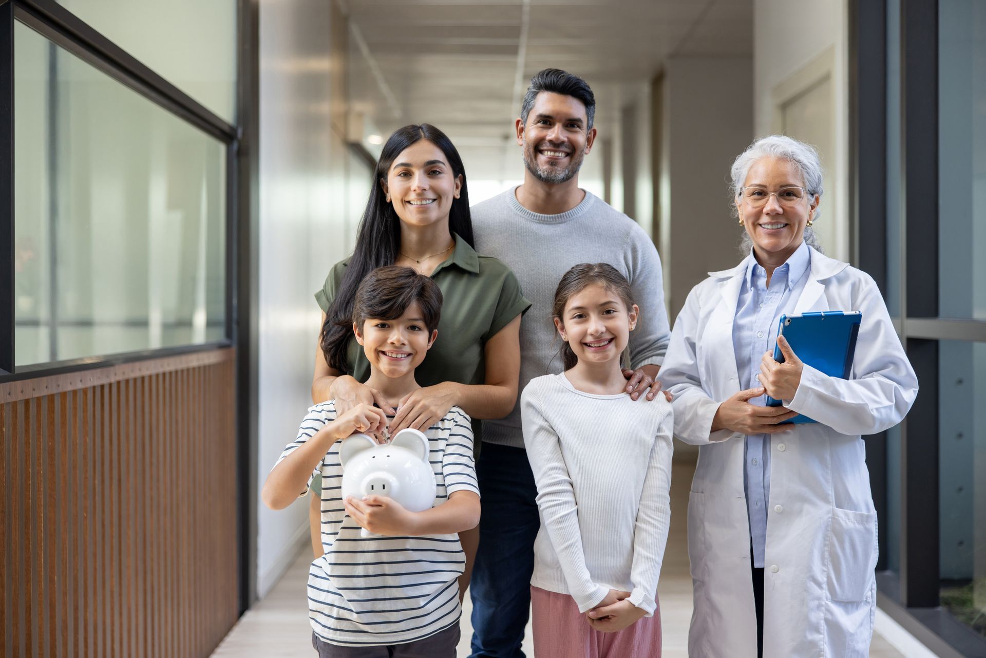 Doctor with family holding piggy bank, smiling together during a clinic visit. Doctor with family holding piggy bank, smiling together during a clinic visit.