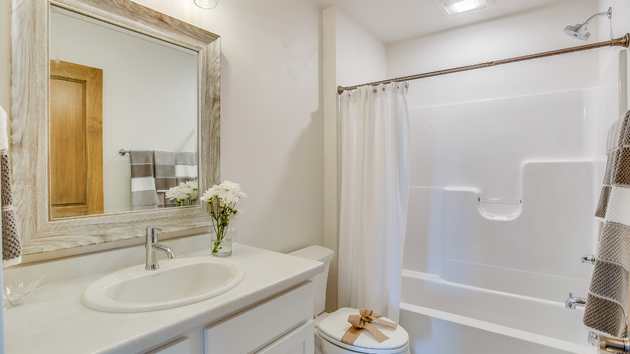 A bright, modern bathroom featuring a white vanity with an oval sink, a large framed mirror, and a white tub-shower combo.