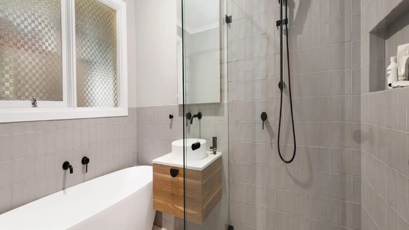 A modern bathroom featuring a white bathtub, a wooden vanity with a vessel sink, and a glass-enclosed shower with grey tiles.