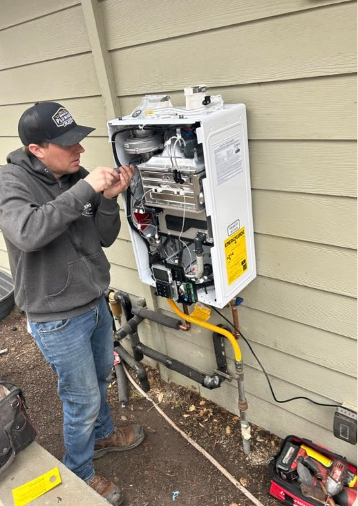 Technician repairing a wall-mounted gas furnace outdoors beside a house.