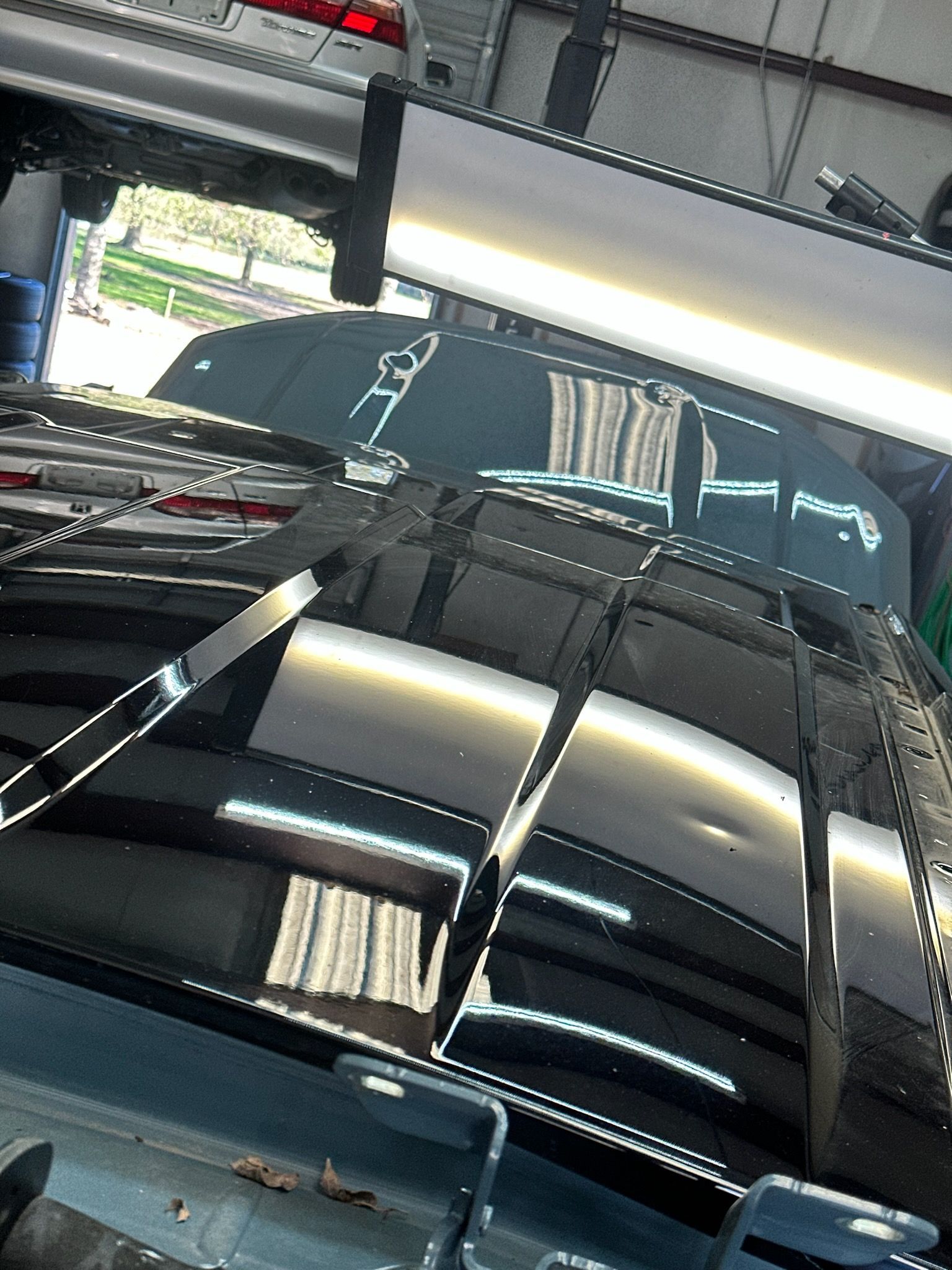 Black car hood with multiple dents under bright repair lights.