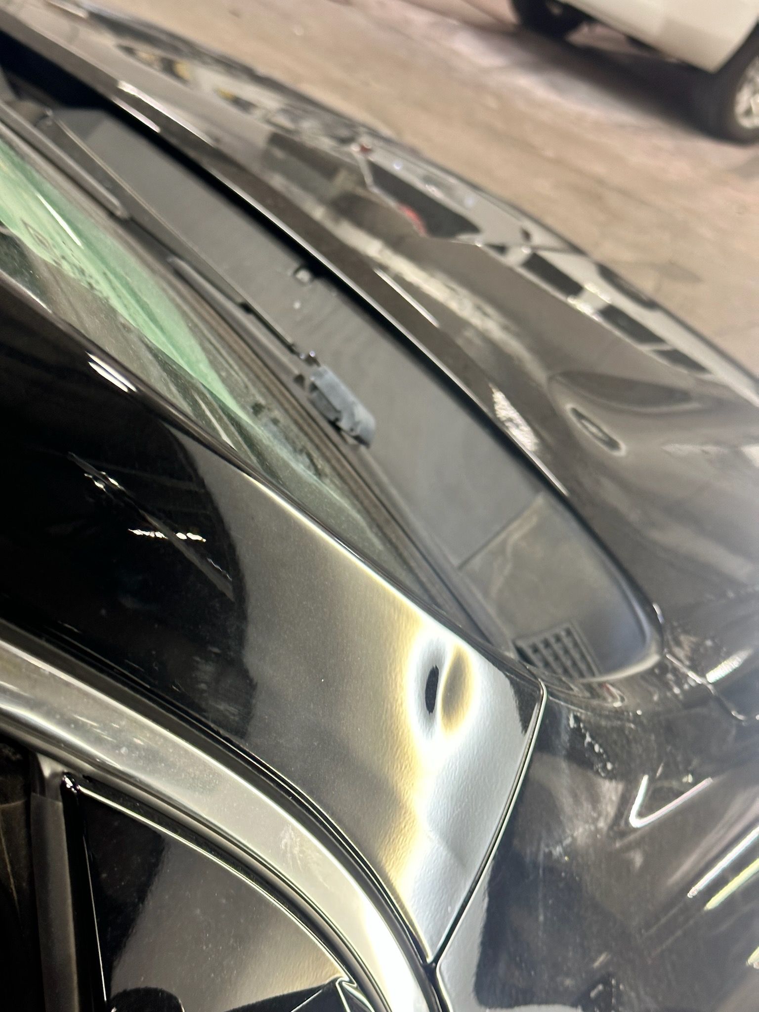 Black car hood with a dent near the windshield wiper, shiny with light reflections.