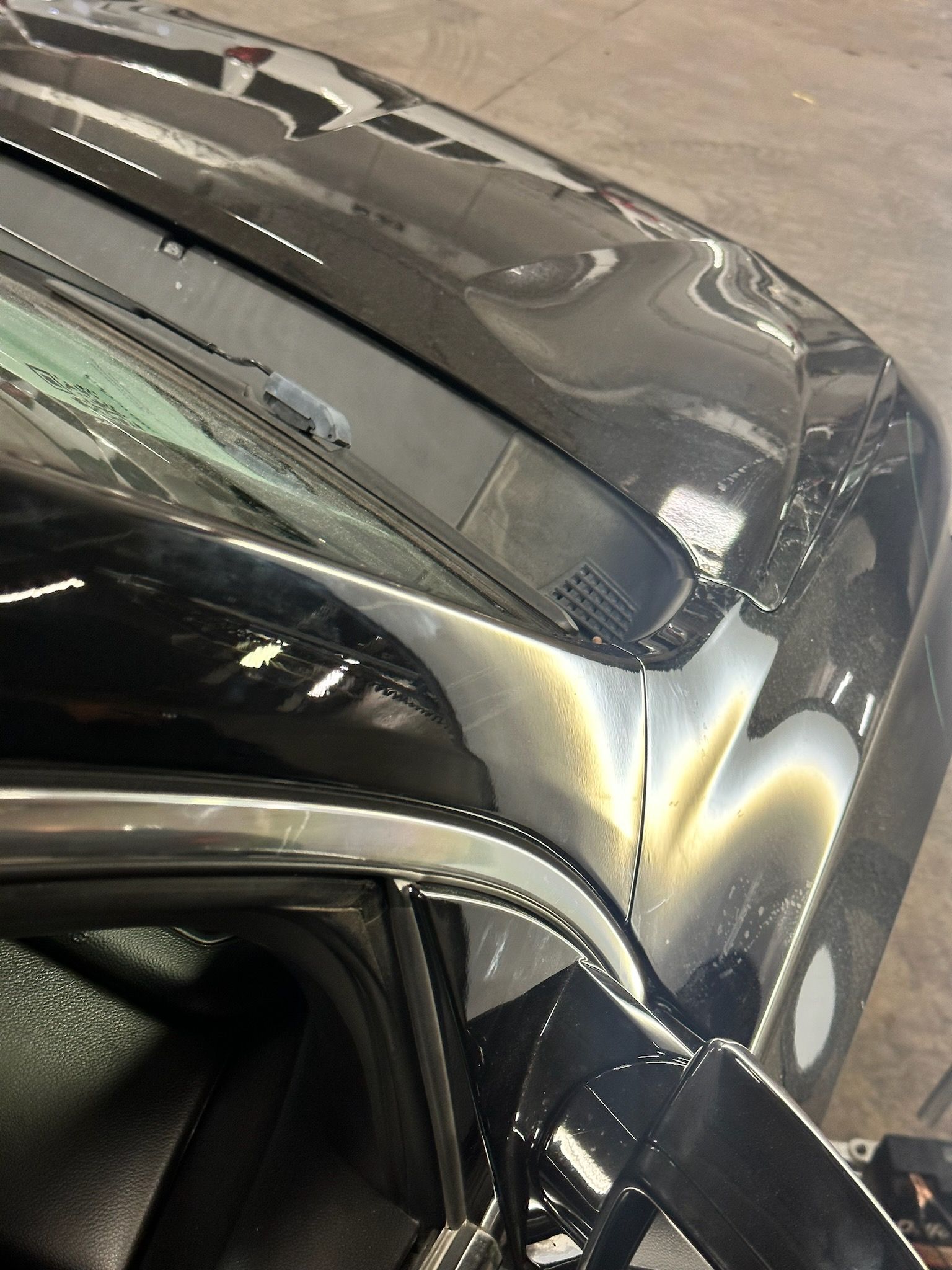 Black car with dents above a window, in a repair shop.