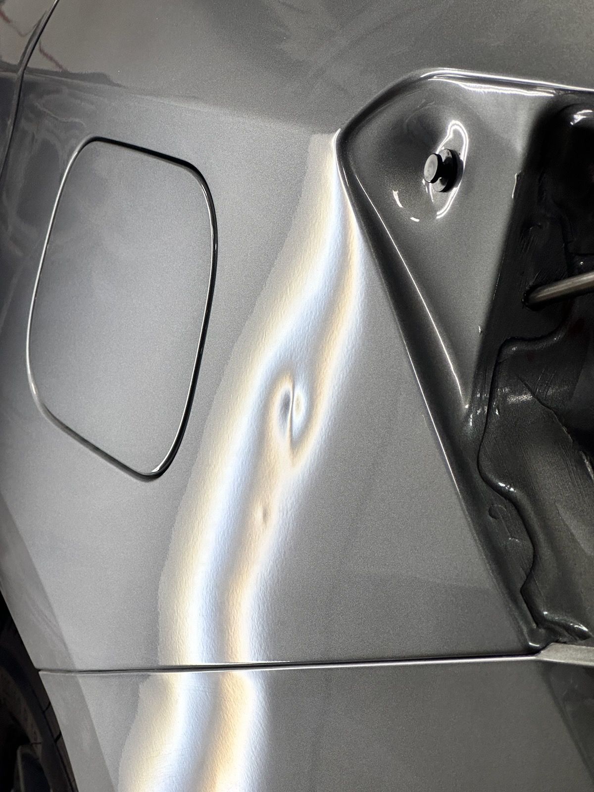 Damaged gray car rear panel with a significant dent near the fuel door and tail light.