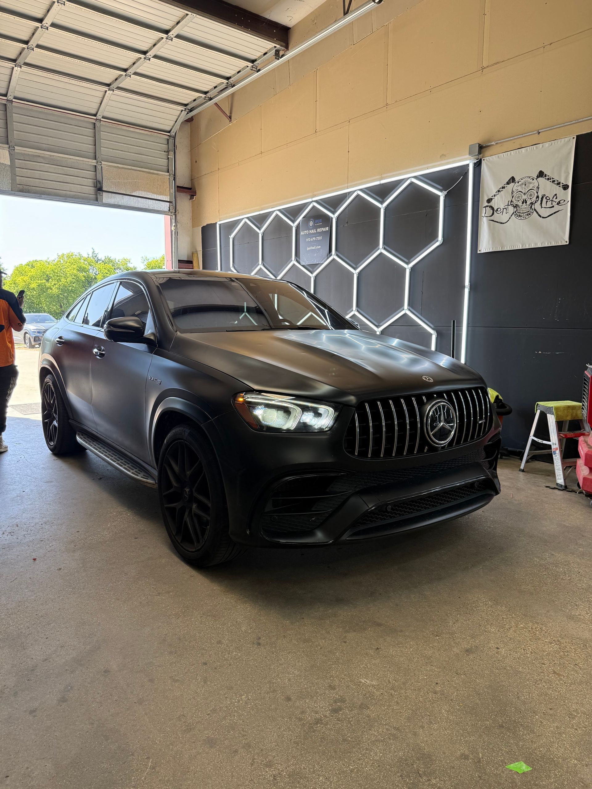 Black matte Mercedes SUV parked in a garage with hexagon-shaped lights on the wall.