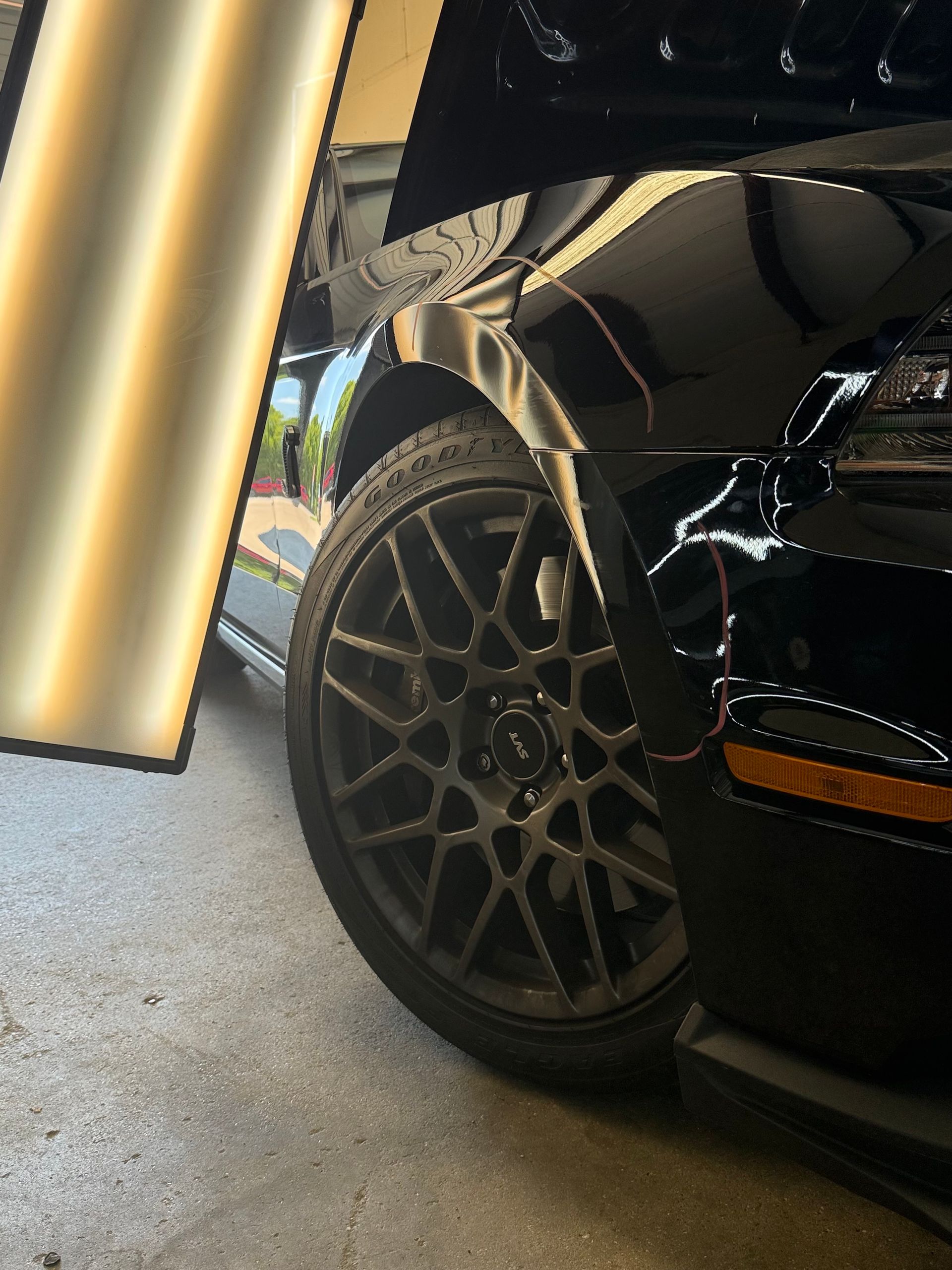 Black car's front tire and fender under bright light, in a garage.