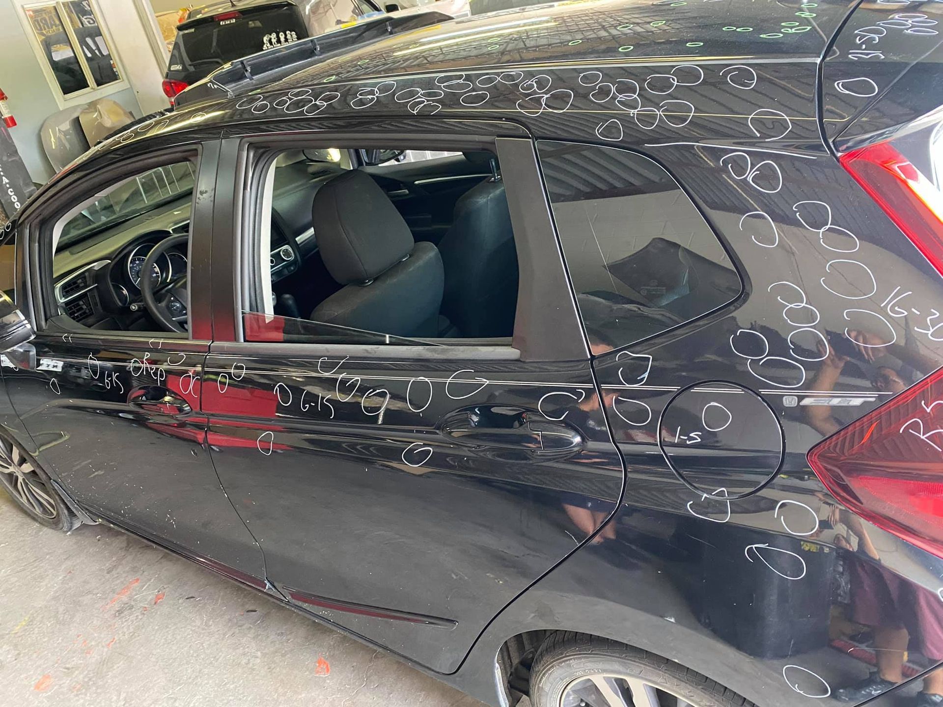 Black Honda Fit with hail damage, parked in a garage.