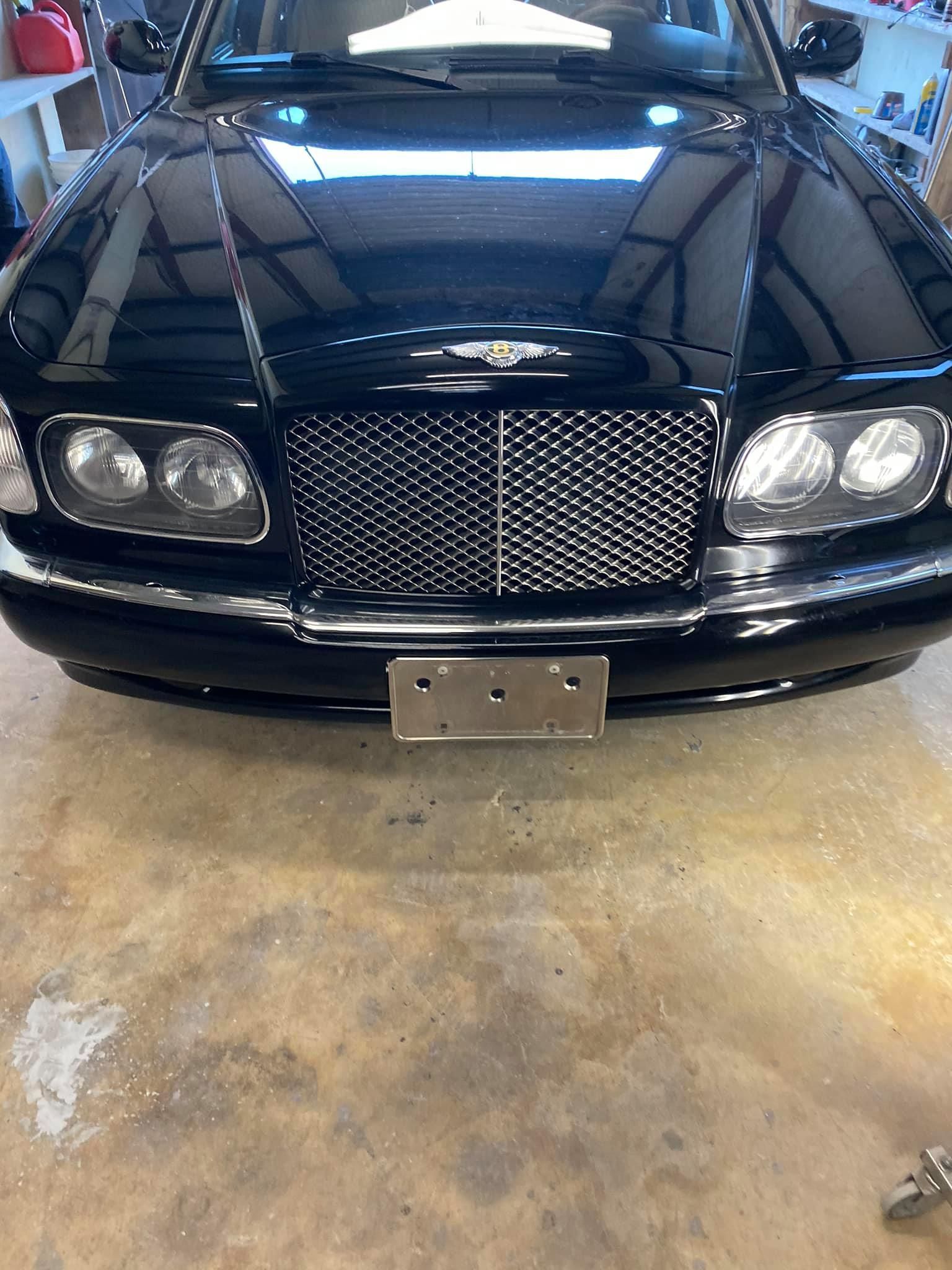 Black Bentley sedan with a silver grille, license plate, and headlights, parked indoors.