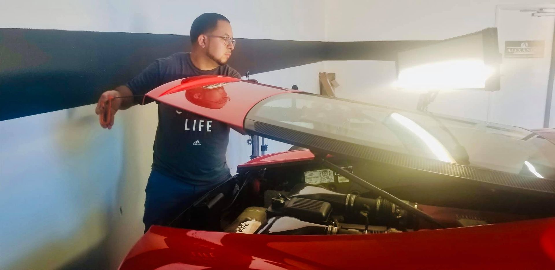 Man looking at the engine of a red car, possibly in a garage.