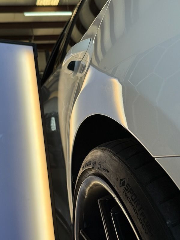 White car's rear quarter panel and tire, lit with a light board to reveal dents.