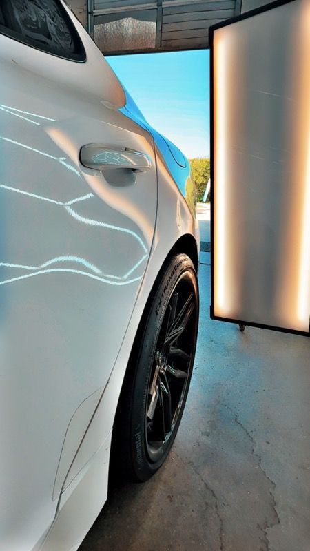 White car side, black wheel, outside. Reflection of lights in the paint.