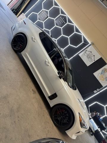 White Kia Stinger sports car with black rims in a garage with honeycomb lighting.