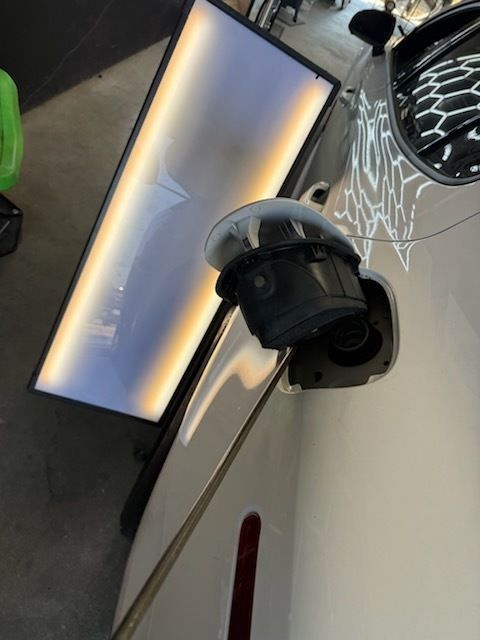 Dent repair on white car near gas cap with specialized lighting.