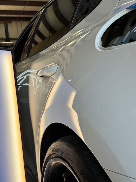 White car with a dent in the rear quarter panel, undergoing dent repair with specialized lighting.