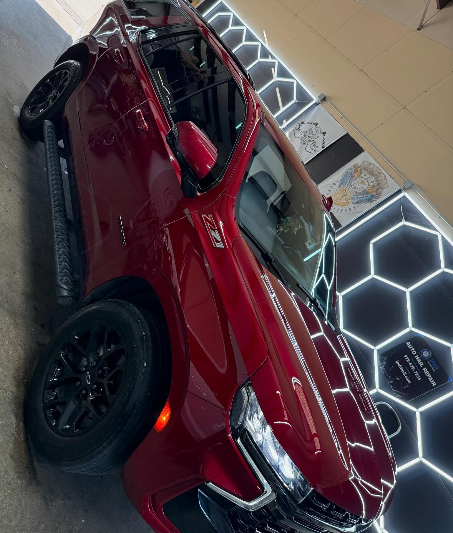 Red SUV parked, shiny, black wheels, near hexagon wall with lights.