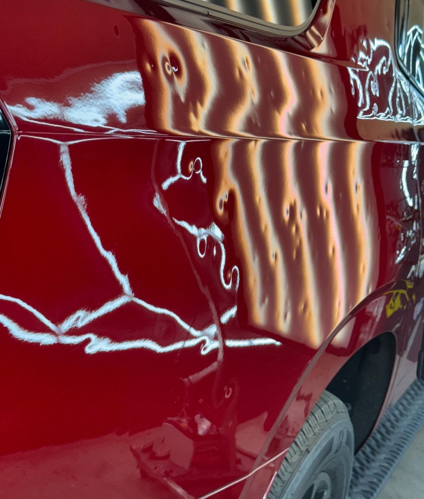 Red vehicle side with multiple dents under bright shop lights.