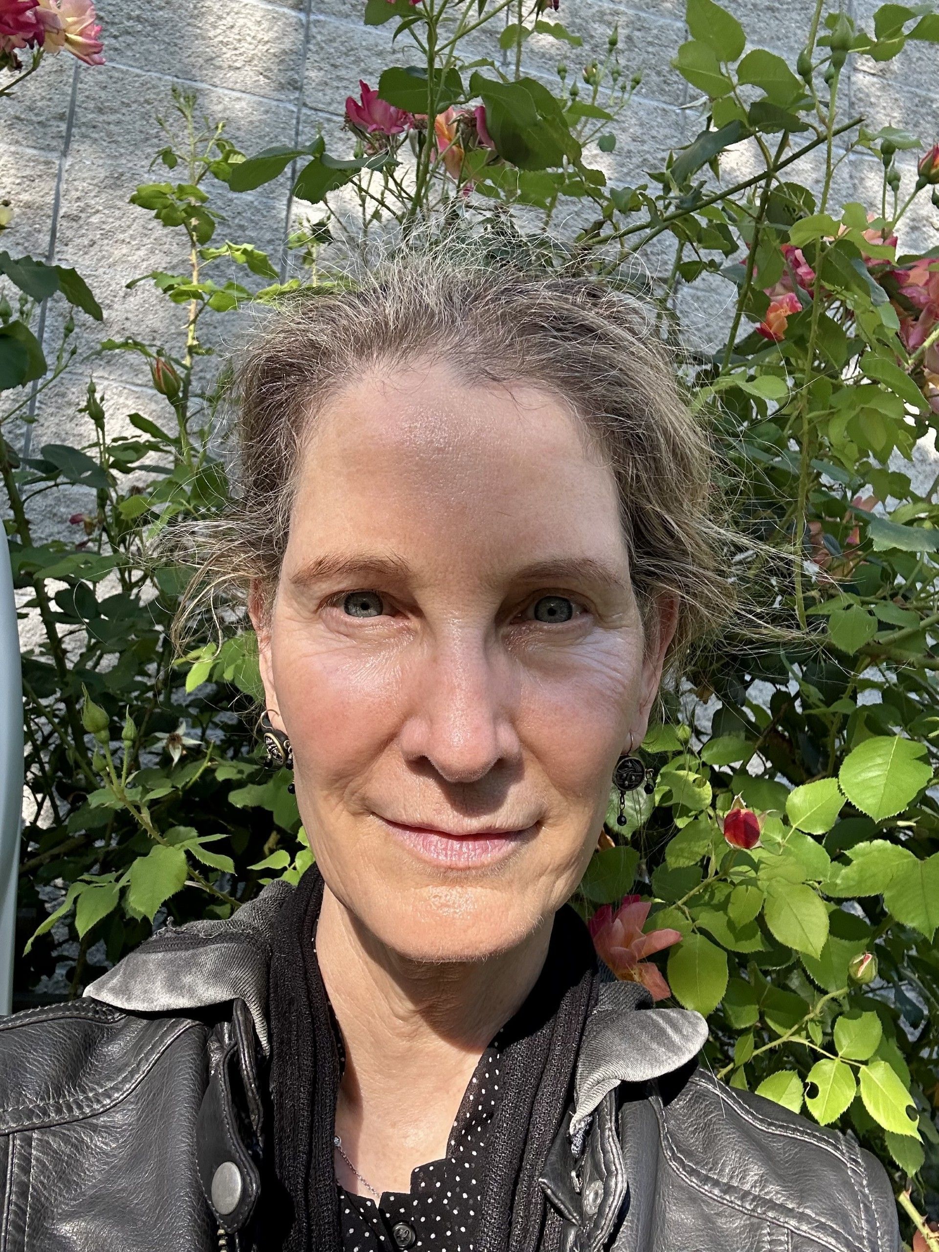 A woman in a black jacket is standing in front of a bush of flowers.
