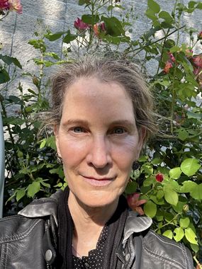 A woman in a black jacket is standing in front of a bush of flowers.