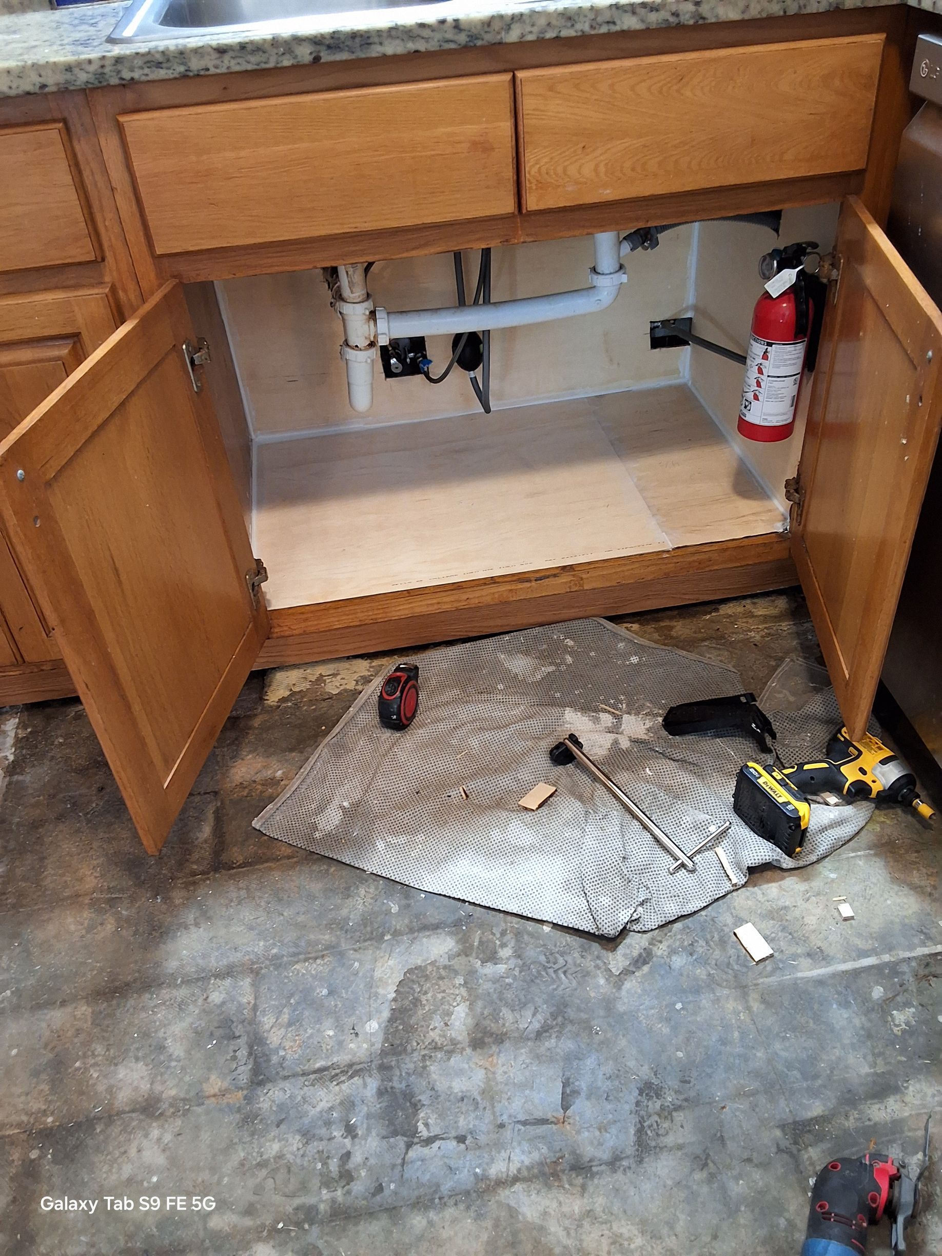 A kitchen sink is being repaired under a cabinet.