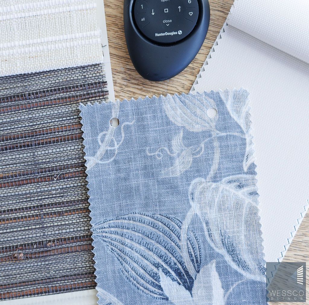 Fabric samples in various textures and patterns, with a remote control on a wooden surface.