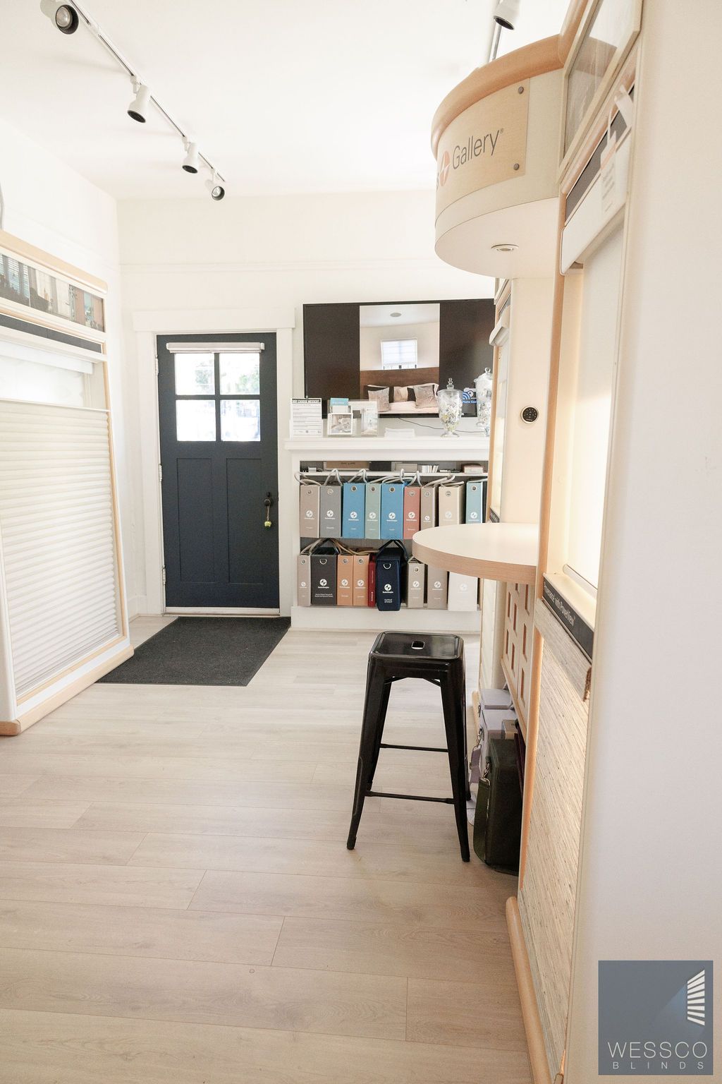 Interior of a showroom with window treatments, a black door, and a black stool.